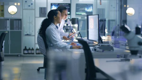 Medical researchers looking at and examining a brain scan on a computer while working late in an office together. Lab workers analyzing and talking about results from a checkup while working overtime